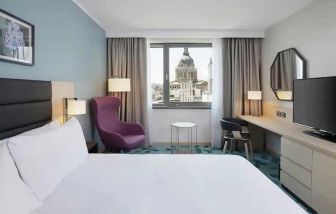 lovely kind bedroom with TV, workspace, couch, and city views at Hilton Garden Inn Budapest City Centre.