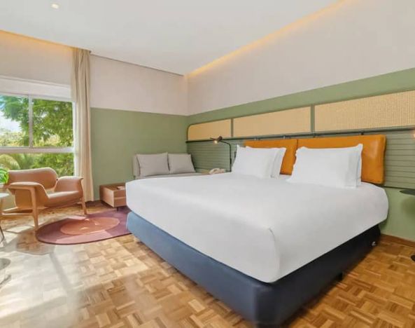Large suite with king-size bed, bright window view, sequenced wood flooring, seating area.