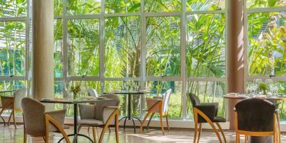 Large windows surrounded by foliage with small circular tables to eat, work, socialize.