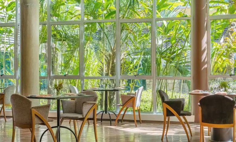 Large windows surrounded by foliage with small circular tables to eat, work, socialize.