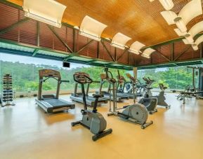 Exercise room with treadmills, ellipticals, space for free weights, with floor to ceiling windows surrounded by view of trees.