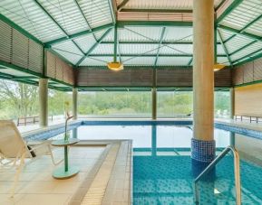 Large pillar in middle of indoor pool with floor to ceiling windows and space to lounge.