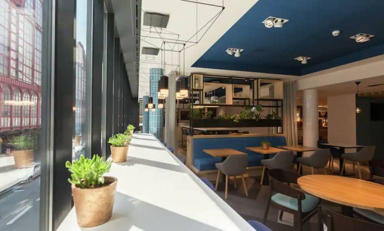 White sunlit table lines window with succulents, other small tables for 1-2 people fill a spacious lobby, perfect for working remotely.