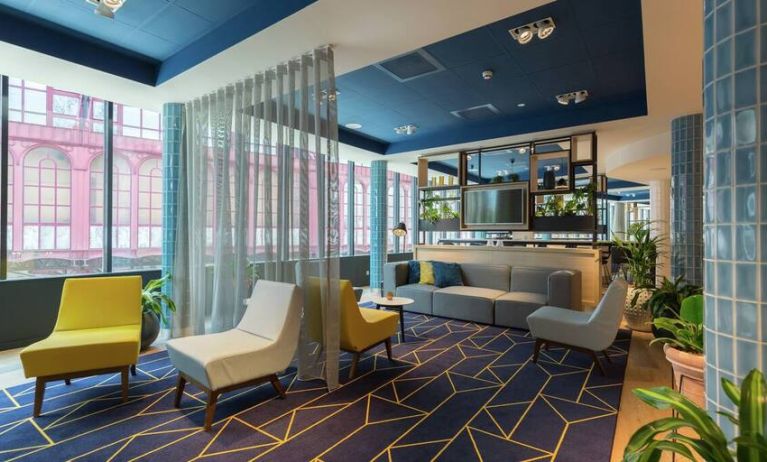 Stylish muted gold and pale blue lounge chairs along with a couch complement a blue and white geometric rug in the Antwerp Hilton lobby.