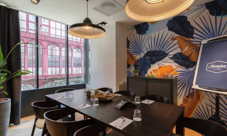 Floral artistic wall pattern and large window view of Antwerp complements a dark brown wooden table and place settings for 8 people to meet and do business in.