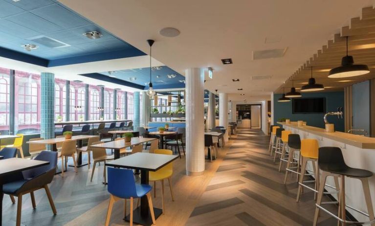 Large lobby with tall ceiling and floor to ceiling window view of downtown Antwerp, various types of seating for socializing, working, eating.