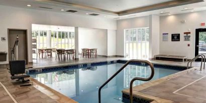 Small rectangular indoor pool with a few circular tables and chairs alongside.