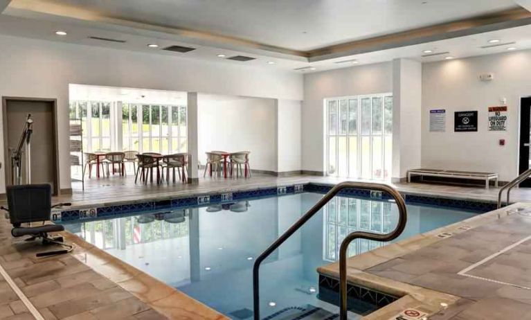 Small rectangular indoor pool with a few circular tables and chairs alongside.