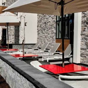 Gray sun layout chairs complement red square tables with chairs on a beautiful outdoor patio at the Hilton Garden Inn Bel Air.