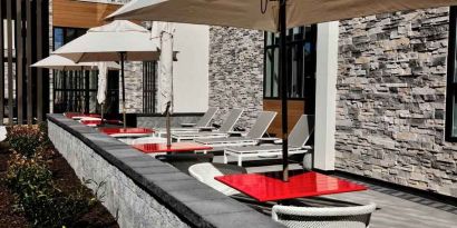 Gray sun layout chairs complement red square tables with chairs on a beautiful outdoor patio at the Hilton Garden Inn Bel Air.