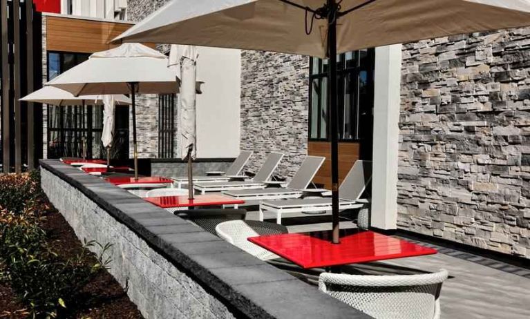 Gray sun layout chairs complement red square tables with chairs on a beautiful outdoor patio at the Hilton Garden Inn Bel Air.