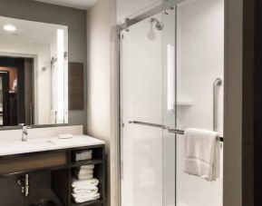 Sliding glass shower doors and large white bathroom vanity space in the day room at Hilton Garden Inn Bel Air.