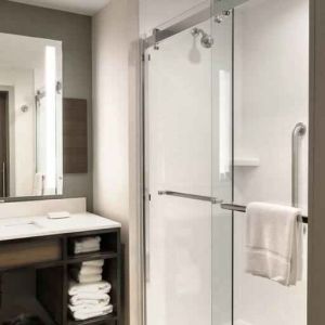 Sliding glass shower doors and large white bathroom vanity space in the day room at Hilton Garden Inn Bel Air.