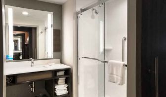 Sliding glass shower doors and large white bathroom vanity space in the day room at Hilton Garden Inn Bel Air.