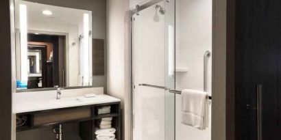 Sliding glass shower doors and large white bathroom vanity space in the day room at Hilton Garden Inn Bel Air.