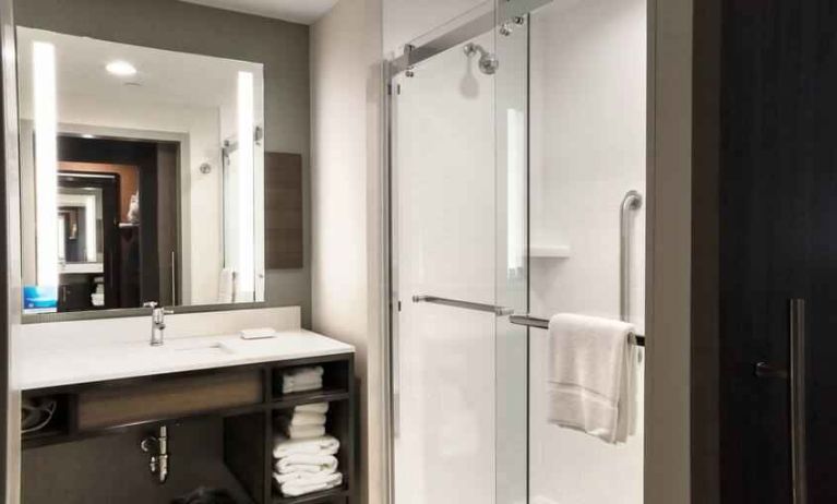 Sliding glass shower doors and large white bathroom vanity space in the day room at Hilton Garden Inn Bel Air.