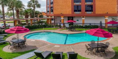 Large outdoor pool with seating area and sun umbrellas at Quality Inn Pasadena.