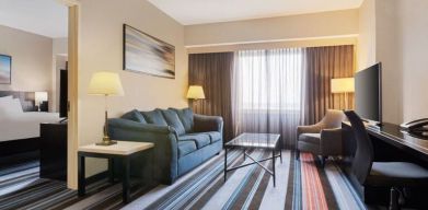 Luxurious king suite with TV, work desk, and couch at Courtyard By Marriott New York JFK Airport.