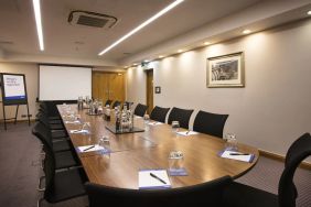 A wider shot of the meeting room with over half a dozen chairs, multiple tables, and a screen.