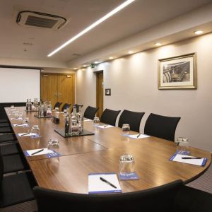 A wider shot of the meeting room with over half a dozen chairs, multiple tables, and a screen.