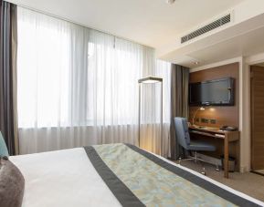 Brightly lit room with king bed and workspace with wall-mounted flat screen TV above.