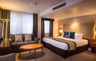 Wide view of the Thistle Trafalgar Square executive king room, featuring large bed, sofa, and TV.