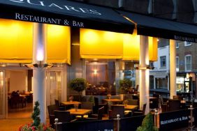 A nocturnal exterior view of the Thistle Trafalgar Square hotel including outdoor seating.