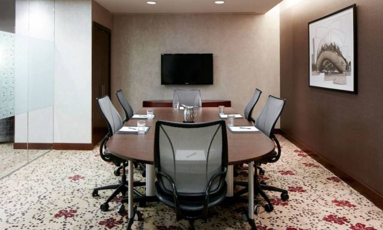 Meeting room in the hotel, with art and TV on the walls and half a dozen chairs arranged around a long table.