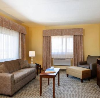 Guest room lounge in Holiday Inn Express Philadelphia Airport, with sofa, chair, TV, and foot stool.