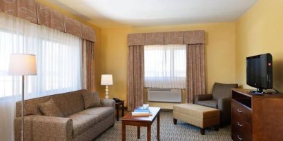 Guest room lounge in Holiday Inn Express Philadelphia Airport, with sofa, chair, TV, and foot stool.