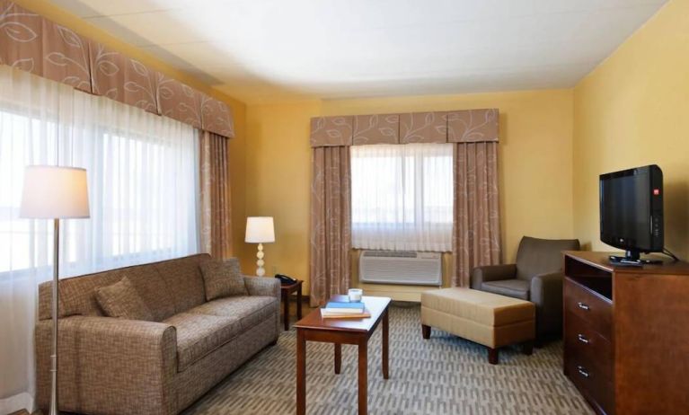 Guest room lounge in Holiday Inn Express Philadelphia Airport, with sofa, chair, TV, and foot stool.