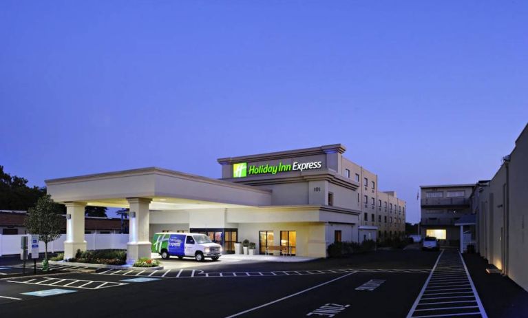 The exterior of the hotel, which provides shade/cover from the rain for the entranceway, and space for parking.