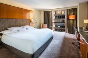 Guest room in Hyatt Regency Chicago, with large double bed, window, and workspace desk, chair, and lamp.