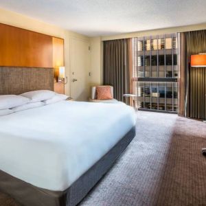 Guest room in Hyatt Regency Chicago, with large double bed, window, and workspace desk, chair, and lamp.