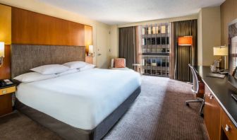 Guest room in Hyatt Regency Chicago, with large double bed, window, and workspace desk, chair, and lamp.