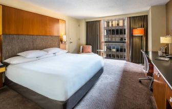 Guest room in Hyatt Regency Chicago, with large double bed, window, and workspace desk, chair, and lamp.