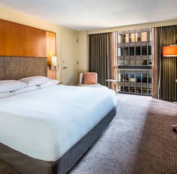 Guest room in Hyatt Regency Chicago, with large double bed, window, and workspace desk, chair, and lamp.