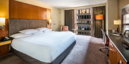 Guest room in Hyatt Regency Chicago, with large double bed, window, and workspace desk, chair, and lamp.