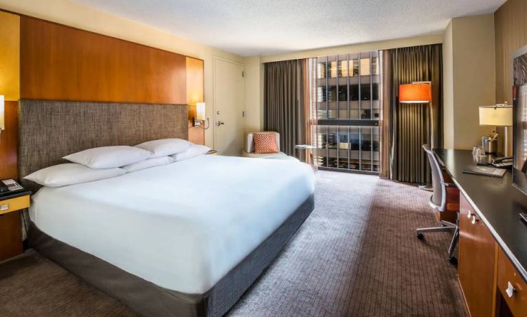 Guest room in Hyatt Regency Chicago, with large double bed, window, and workspace desk, chair, and lamp.