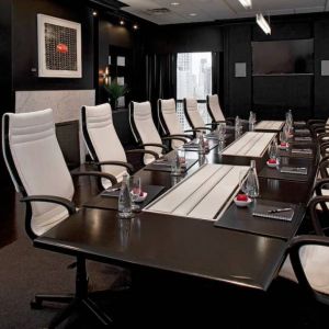 Stylishly dark meeting room, with long black table and white chairs around it.