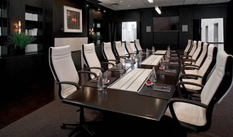 Stylishly dark meeting room, with long black table and white chairs around it.