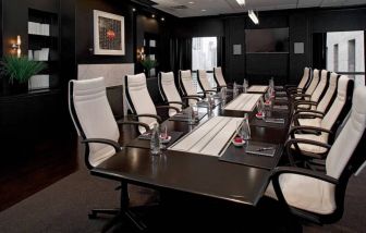 Stylishly dark meeting room, with long black table and white chairs around it.