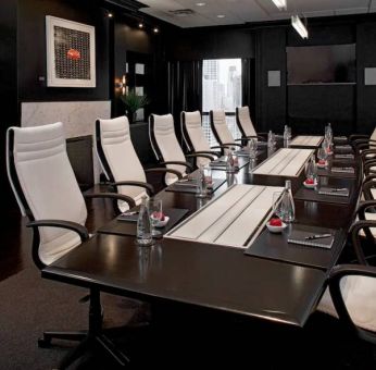 Stylishly dark meeting room, with long black table and white chairs around it.