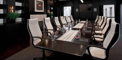 Stylishly dark meeting room, with long black table and white chairs around it.