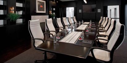 Stylishly dark meeting room, with long black table and white chairs around it.