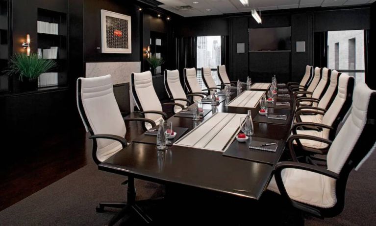 Stylishly dark meeting room, with long black table and white chairs around it.