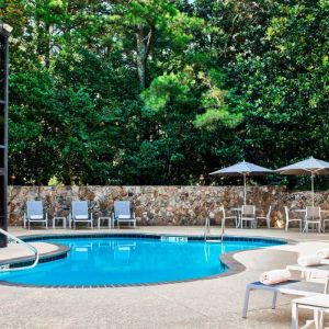 The hotel’s outdoor swimming pool has surrounding loungers and nearby trees.