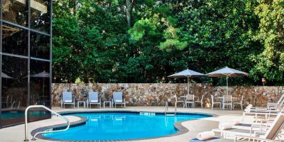 The hotel’s outdoor swimming pool has surrounding loungers and nearby trees.