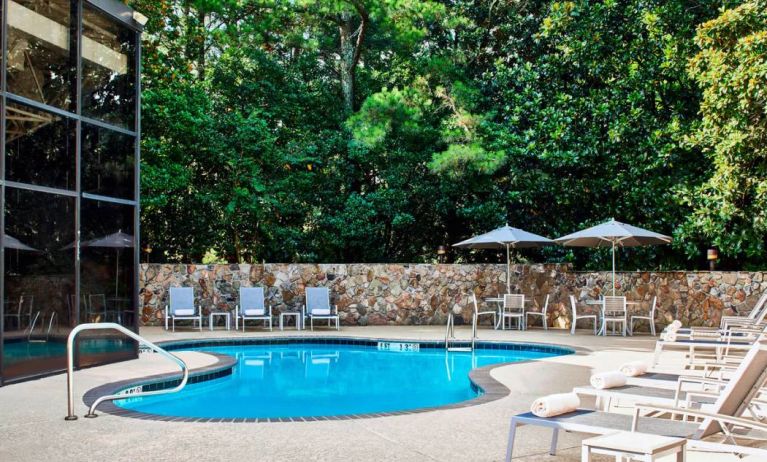 The hotel’s outdoor swimming pool has surrounding loungers and nearby trees.