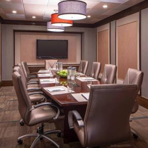 Hotel meeting room, featuring long wooden table and surrounding leather chairs.